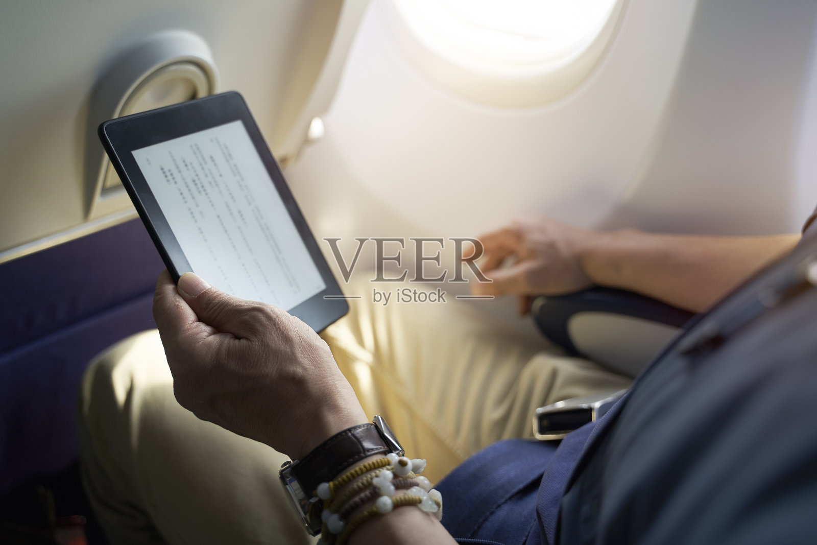 一名亚洲男子在飞机上使用电子阅读器阅读照片摄影图片