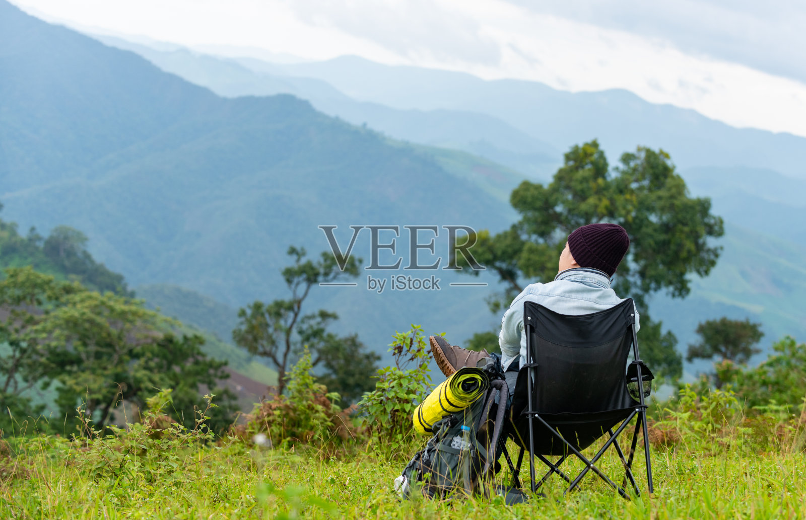 快乐的亚洲人背包客坐在户外的椅子放松在美丽的自然山草地在夏天的一天。寂寞的帅哥享受与户外的生活方式度假照片摄影图片