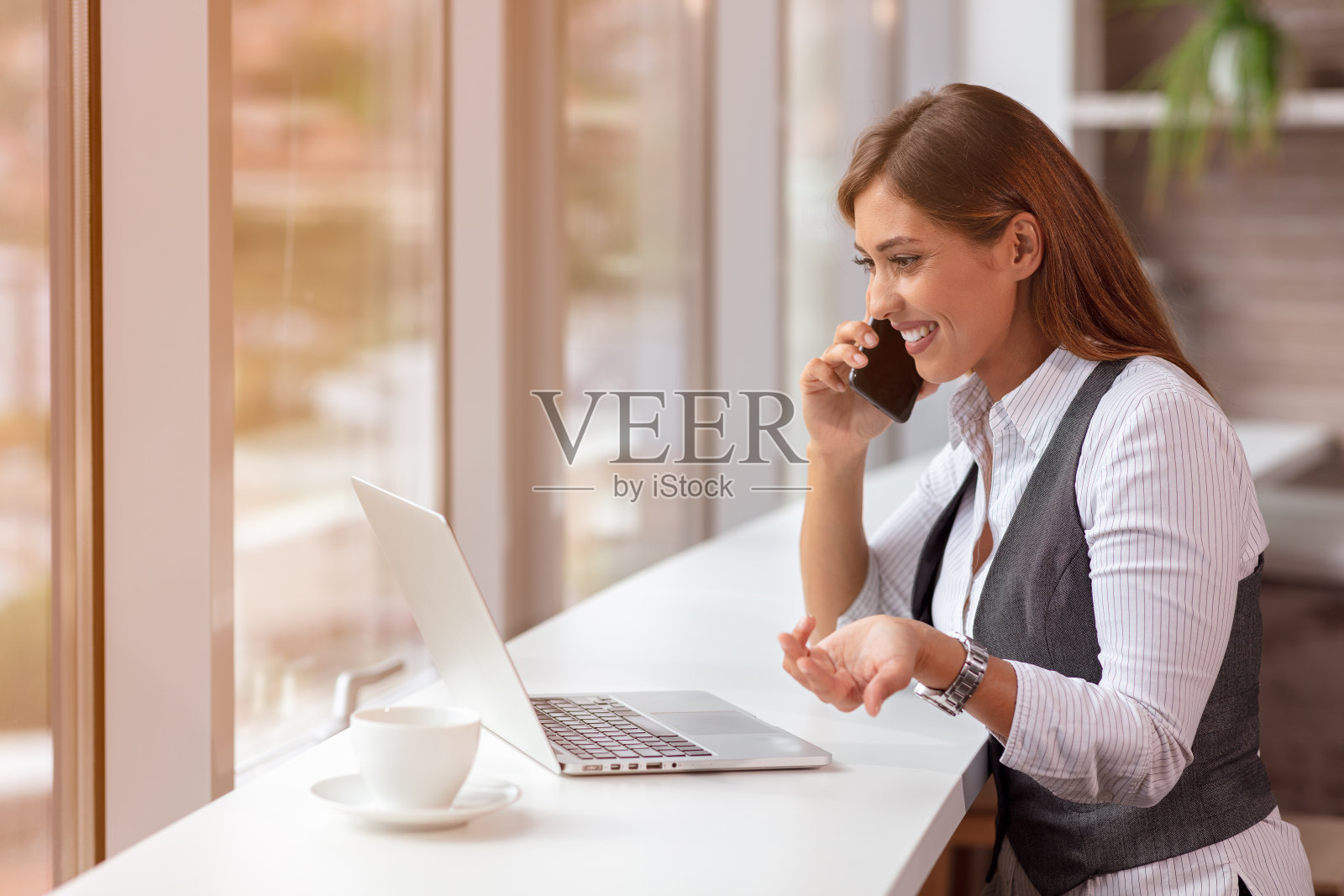 一个年轻的女人在室内用电脑和智能手机，在办公室工作。照片摄影图片