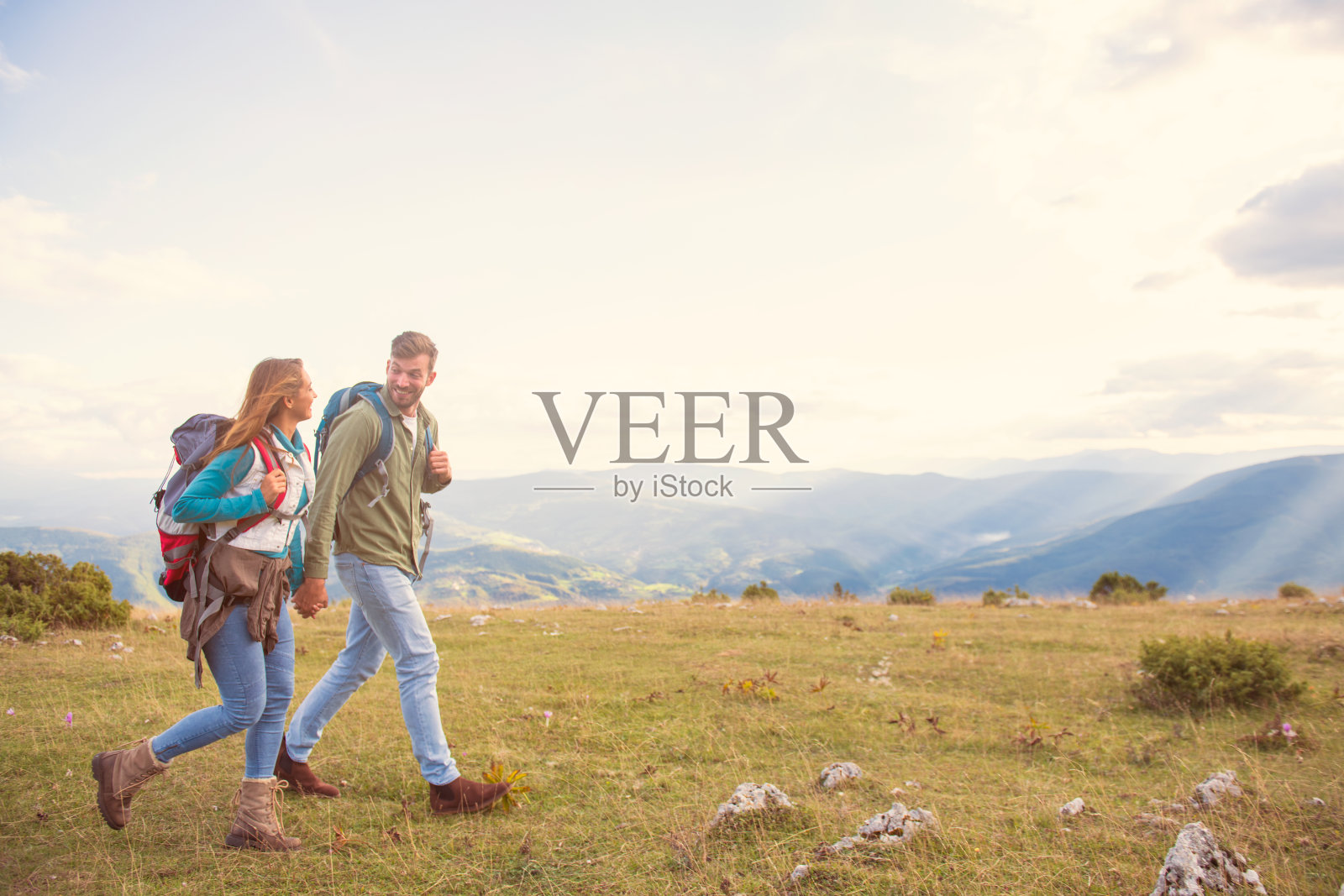 一对年轻夫妇在山里背包旅行，享受他们的生活。侧视图与大美丽的山在背景。照片摄影图片
