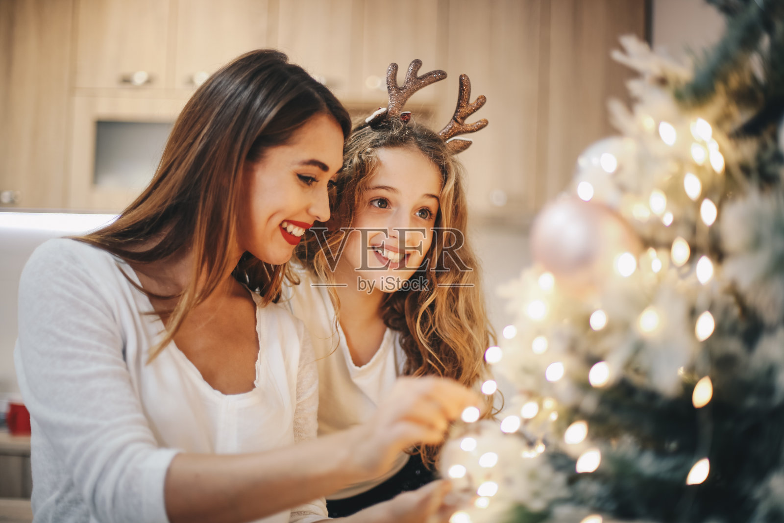 两个女孩高兴地打开圣诞树上的灯。照片摄影图片