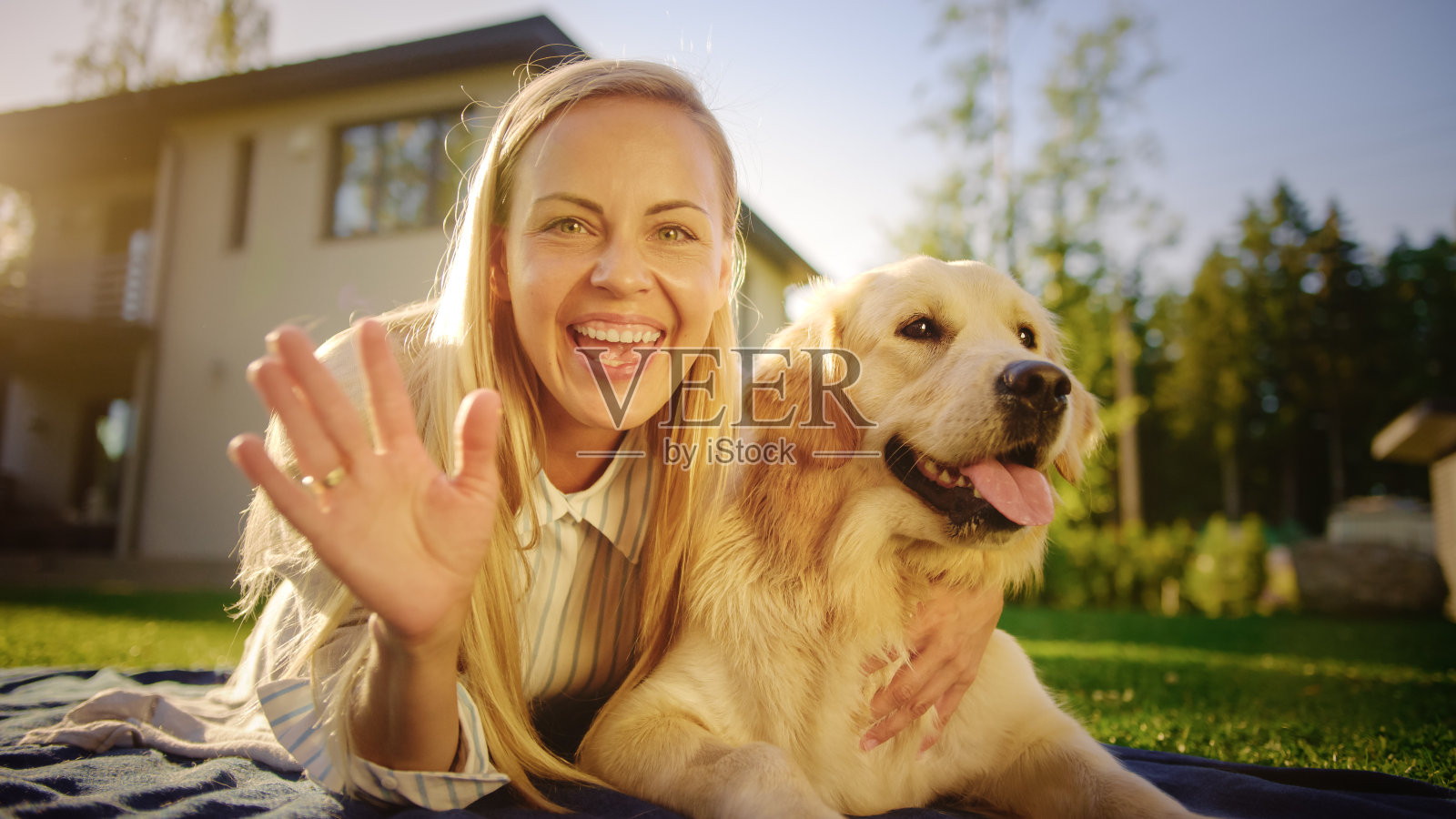年轻美丽的女人在户外野餐拥抱她的金毛纯种狗，向相机打招呼。与亲友交谈。POV视频电话会议概念照片摄影图片