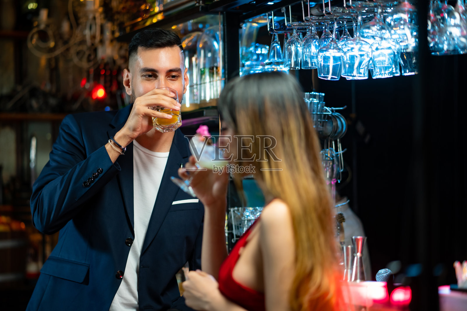 英俊的白人男子站在酒吧柜台调情，与美丽的女人聊天，享受酒精鸡尾酒在夜总会聚会。微笑的情侣在酒吧享受浪漫的约会。照片摄影图片