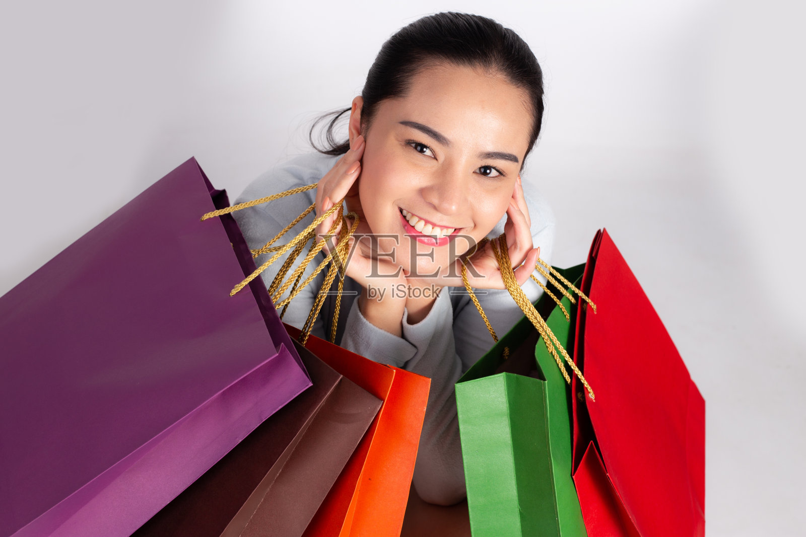 开朗美丽的亚洲女人拿着多种颜色的购物袋和显示ok标志在浅白色的背景。照片摄影图片