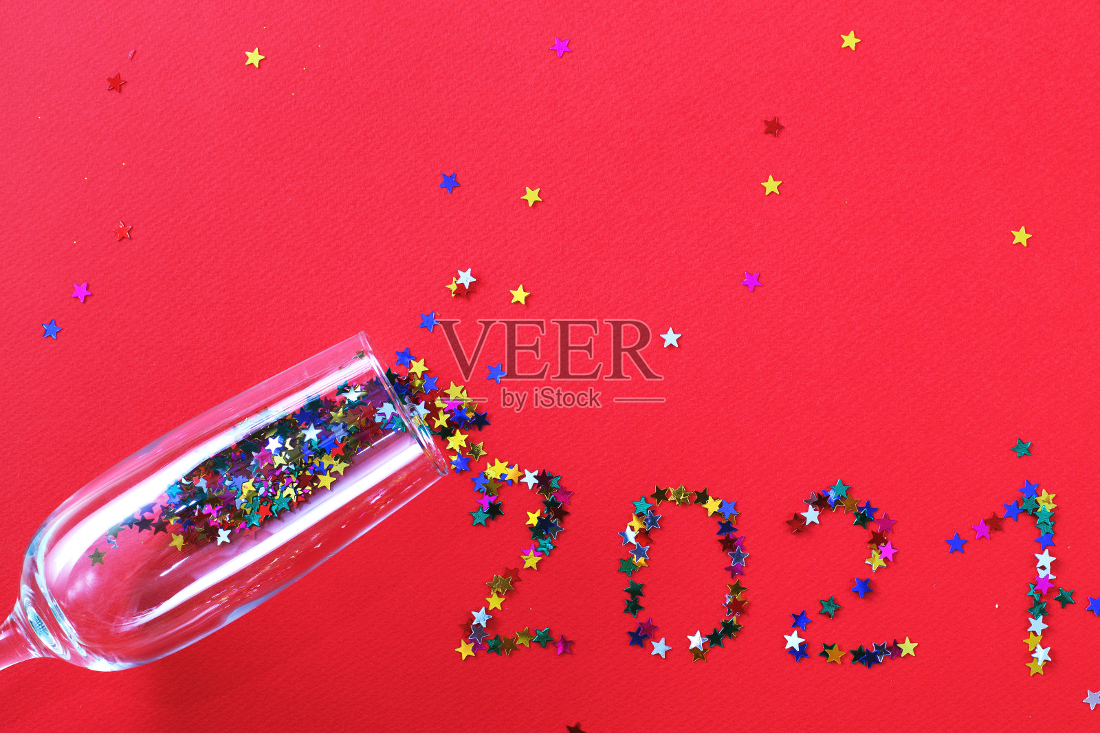 红色背景上点缀着星形亮片的香槟酒杯上的“2021”字样。照片摄影图片
