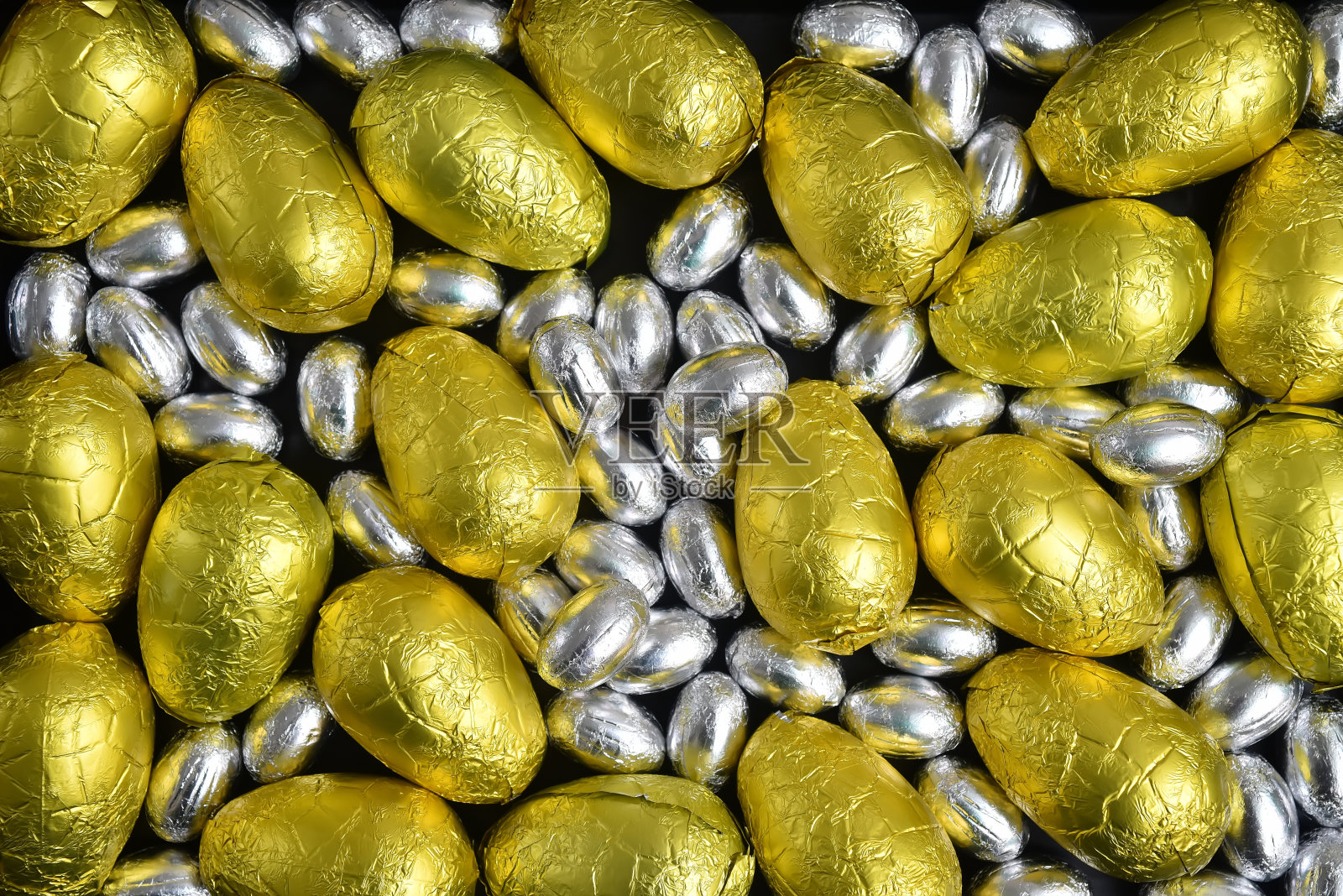 大、小、黄、金、银箔包裹的巧克力复活节彩蛋，以黑色为背景。照片摄影图片