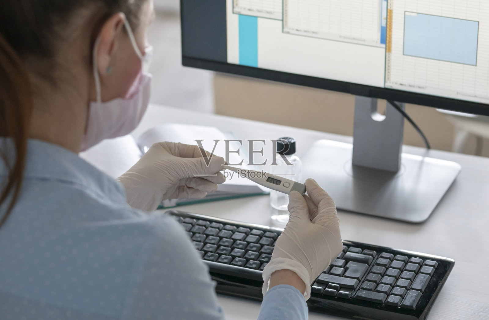 一名无法辨认的女患者手持智能手机和体温计，使用笔记本电脑进行家庭隔离隔离Covid-19大流行冠状病毒。照片摄影图片
