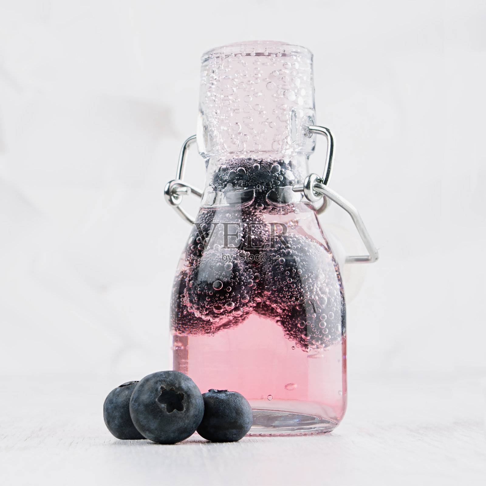 天然有机粉红鸡尾酒蓝莓，碳酸水轭瓶在明亮的白色木板和墙壁，方形。照片摄影图片
