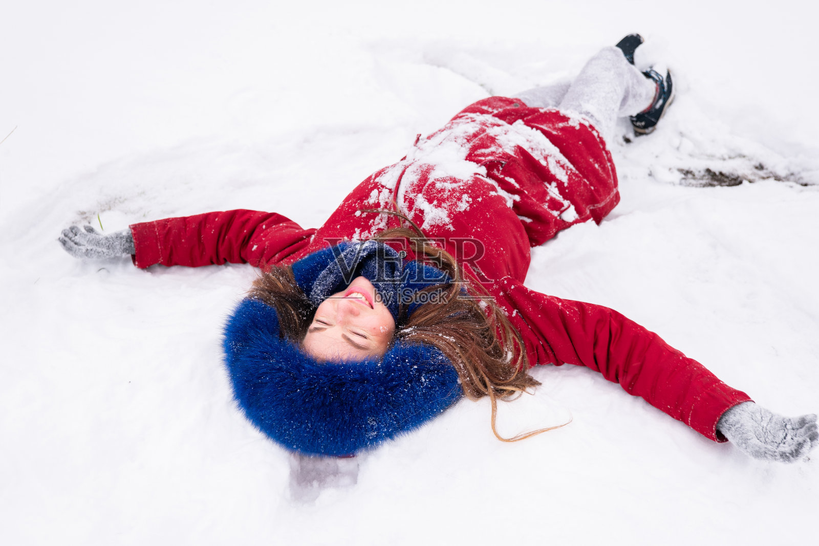 年轻快乐的女人穿着红色外套躺在雪地上照片摄影图片