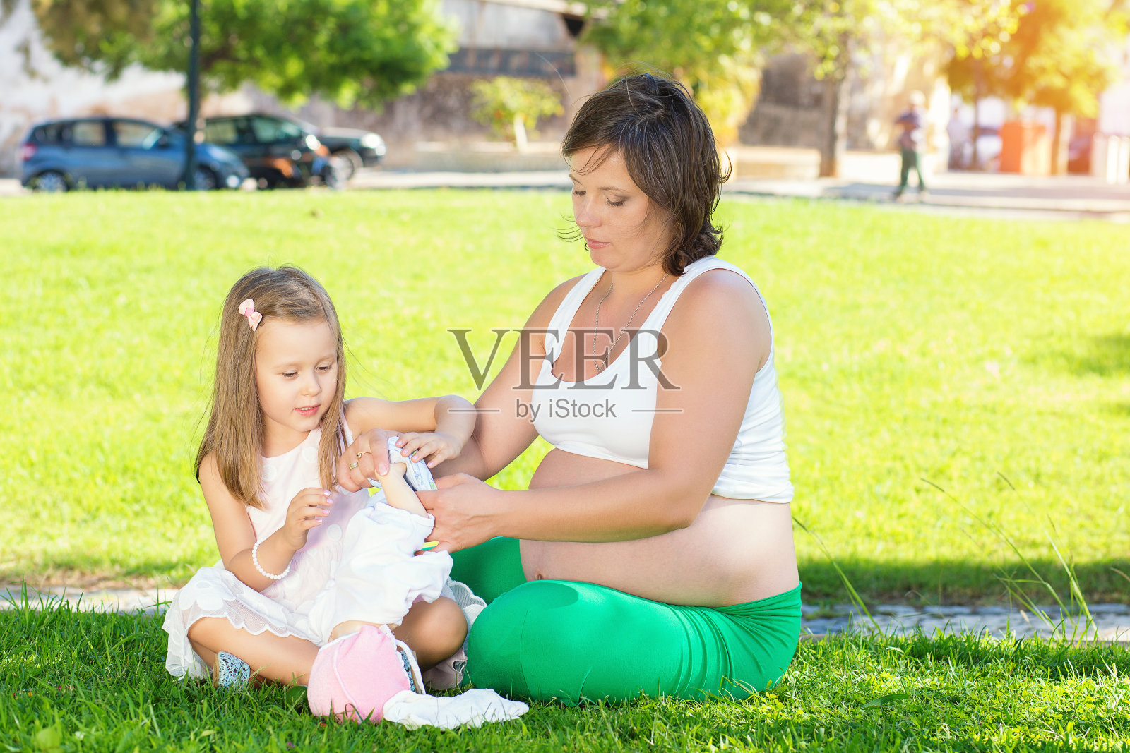 小女孩和怀孕的妈妈在公园的绿色草地上休息玩耍照片摄影图片