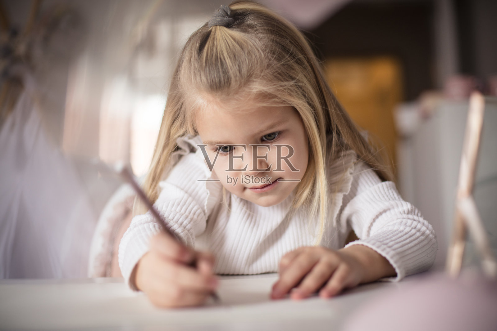 小女孩坐在她的房间里写作。照片摄影图片