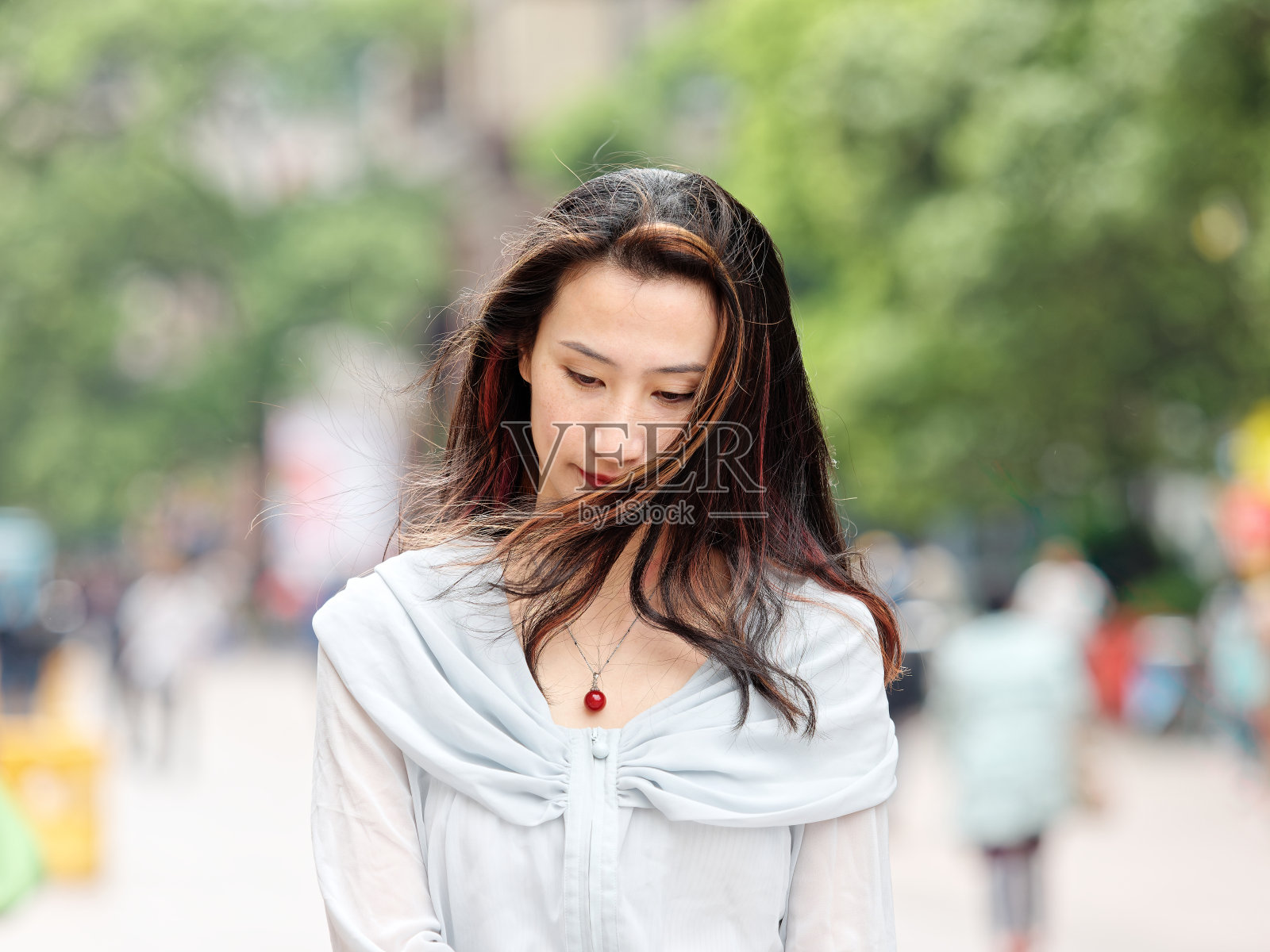 在刮风的日子里，美丽的女人低着头走在上海的南京路上。照片摄影图片