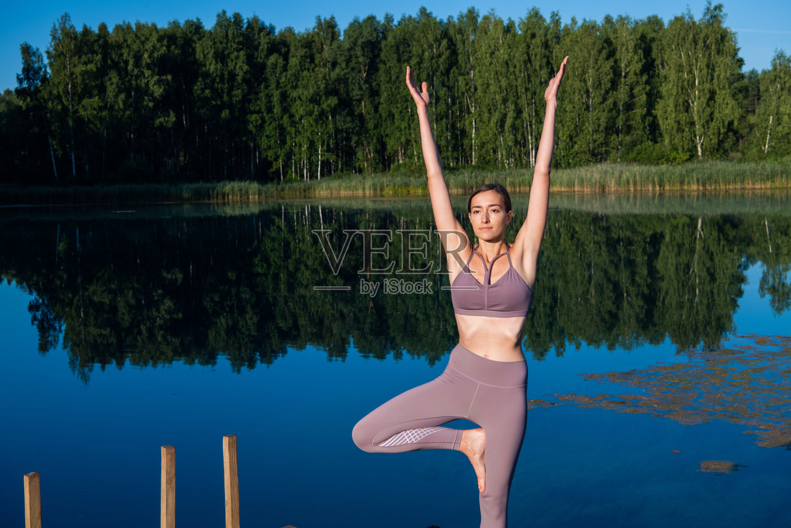 女孩在大自然中做瑜伽树姿势。女孩瑜伽姿势。户外运动伸展在森林湖上照片摄影图片