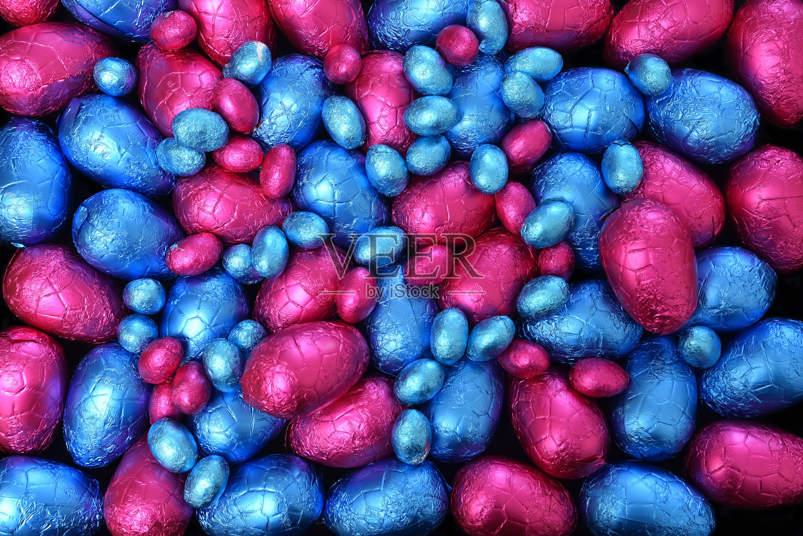 一堆或一组多颜色和不同大小的彩色铝箔包装的巧克力复活节彩蛋在蓝色和粉红色。照片摄影图片