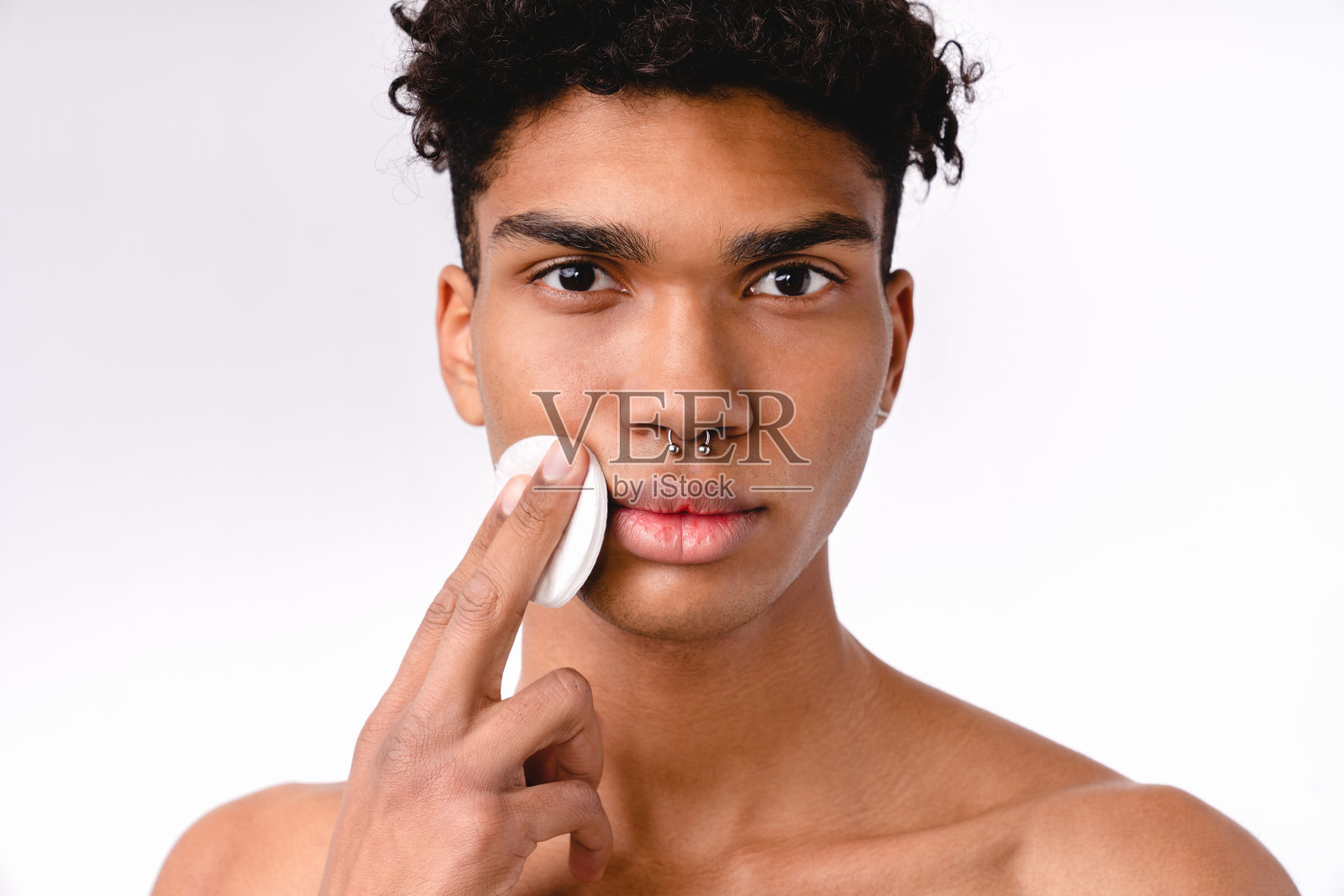 一名年轻的非洲男子使用棉垫，赤裸上身，背景为白色照片摄影图片