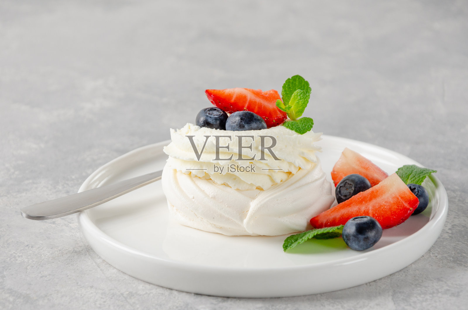 灰色混凝土背景上的盘子上有一个迷你的巴芙洛娃蛋白蛋糕，上面有鲜奶油和新鲜的浆果。夏天的甜点。副本的空间。照片摄影图片