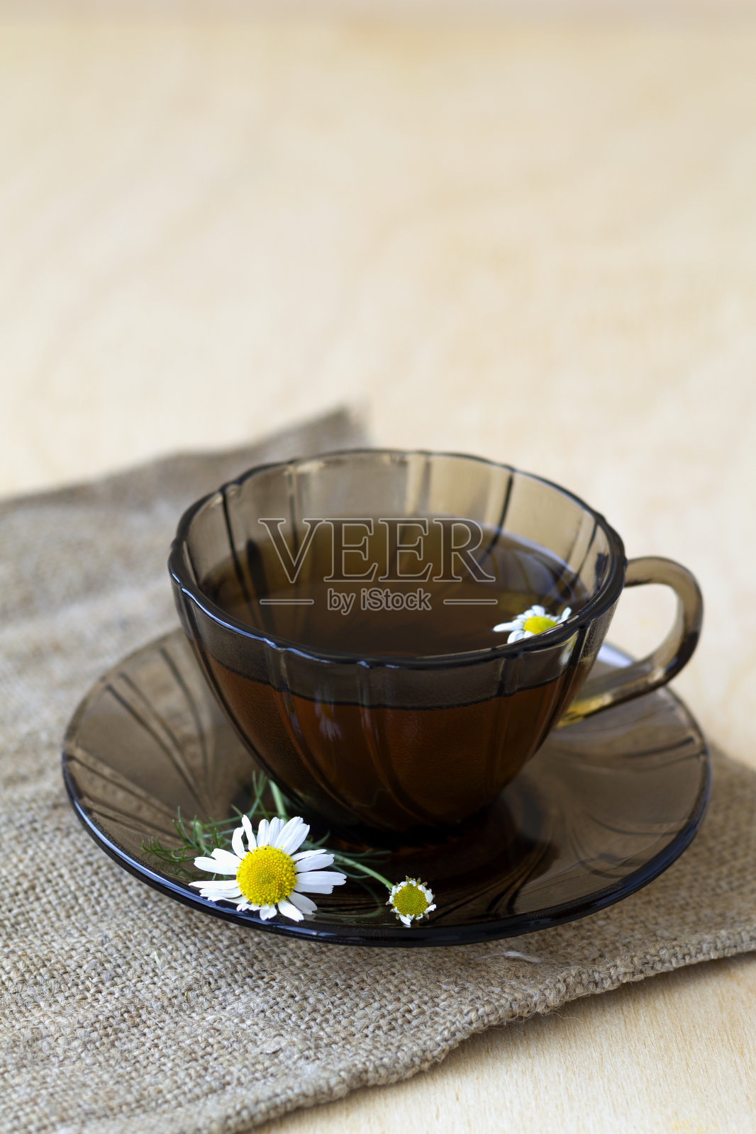 在一张有复印空间的轻木桌上，用麻布铺着一杯凉茶和甘菊茶。一杯鲜花绿叶的茶，黄底，垂直照片摄影图片