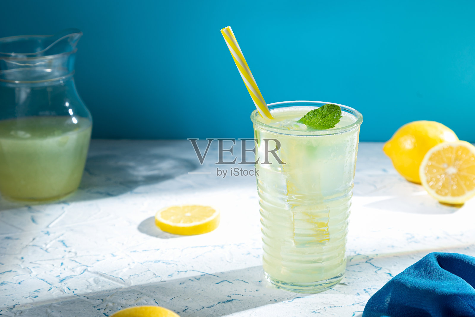 玻璃杯里有柠檬水和柠檬，背景是蓝光。照片摄影图片