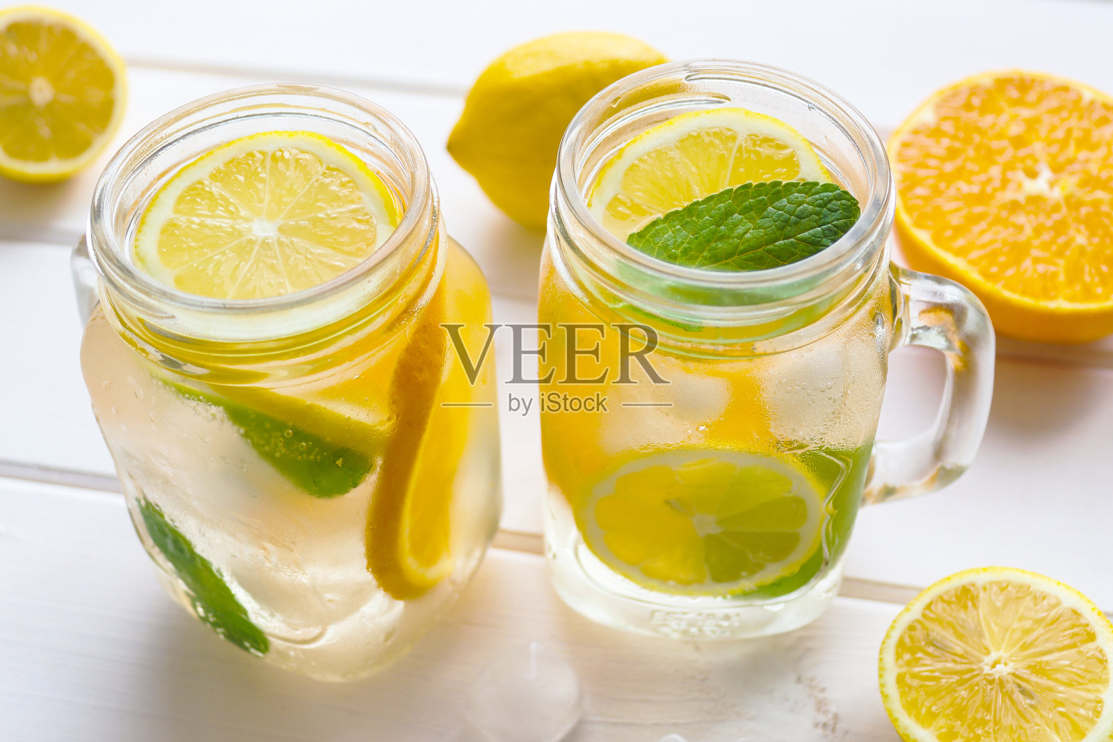白色的木桌上放着新鲜的柠檬、橘子、薄荷和冰。夏季清凉饮料。特写,有选择性的重点照片摄影图片