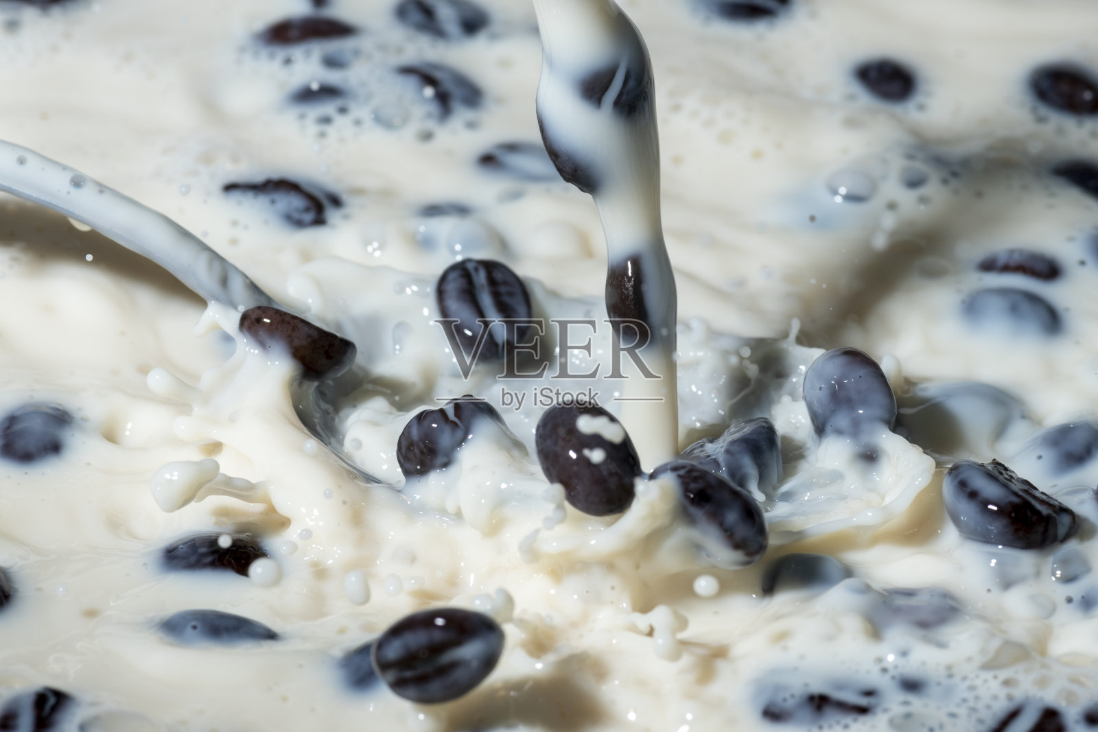 咖啡豆落在牛奶上溅起水花。照片摄影图片