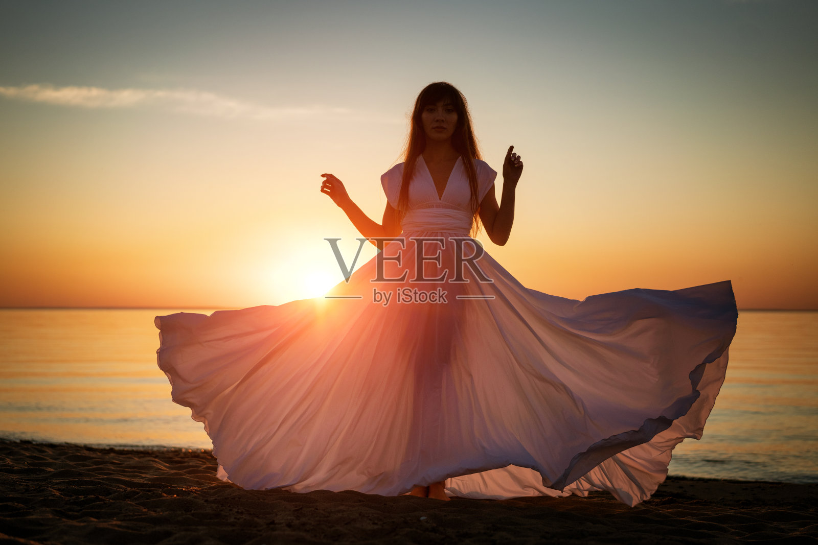 日落时分，美丽的女性剪影穿着白色长裙站在海边照片摄影图片