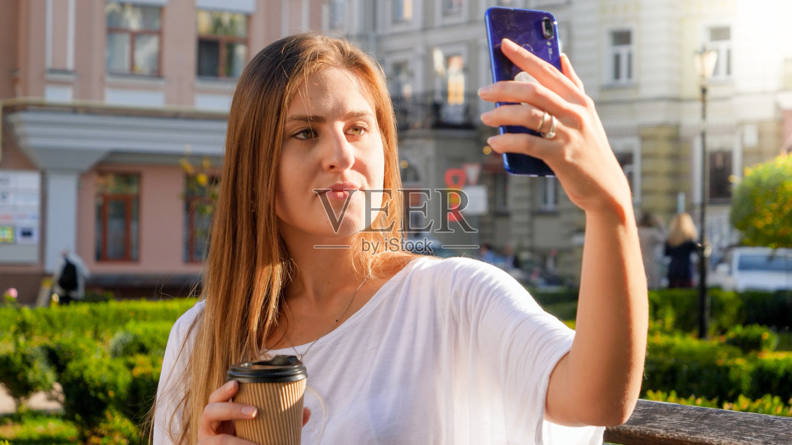 肖像为时尚的年轻女子在公园的长凳上用手机自拍照片摄影图片