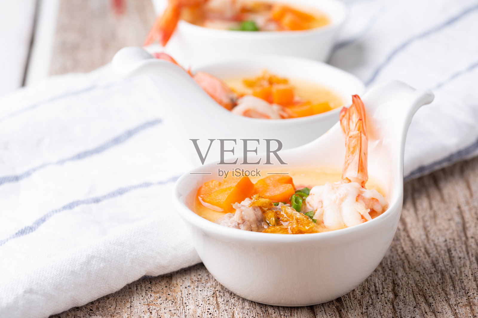 木桌上的瓷碗里放着自制的虾和蔬菜蒸蛋。健康食品的概念。照片摄影图片
