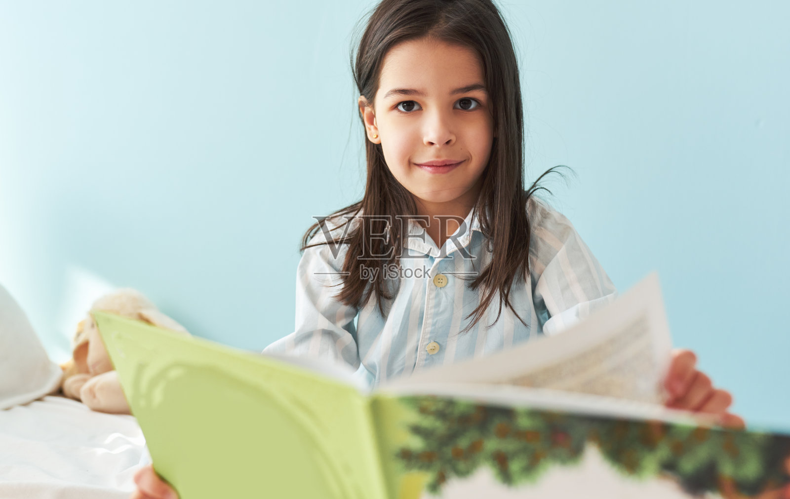 一个可爱的小女孩坐在床上读童话书的肖像。快乐的孩子穿着睡衣在舒适的床上读有趣的故事在早上在家里。照片摄影图片