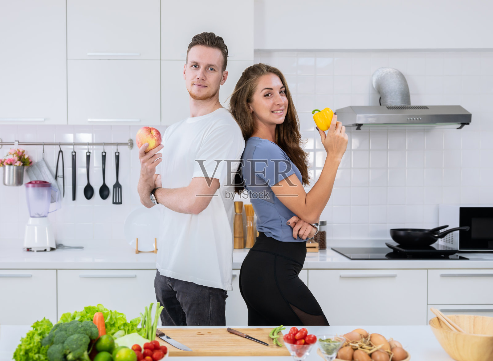 幸福的情侣在厨房一起做饭。年轻的男男女女站在那里，手里拿着新鲜的水果和蔬菜照片摄影图片
