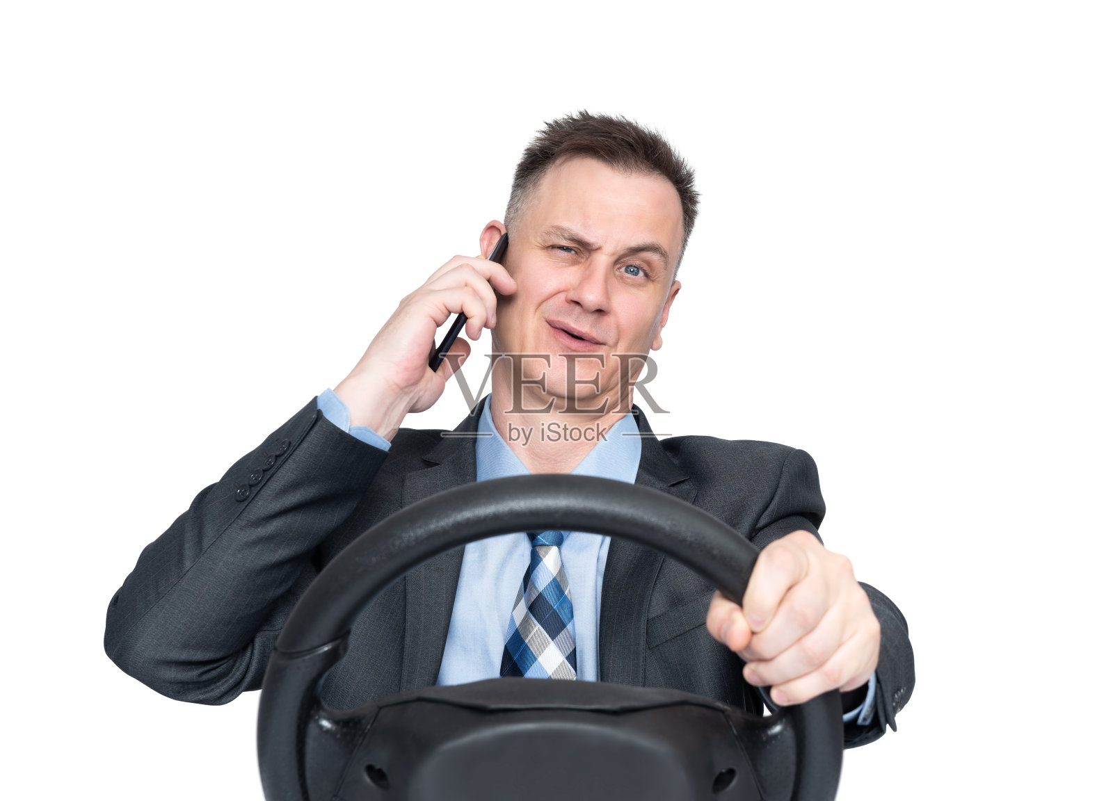 一名身穿深色西装、打着领带的男子正在用智能手机讲话，手里拿着汽车方向盘，在白色背景中孤立无间。安全驾驶的概念照片摄影图片