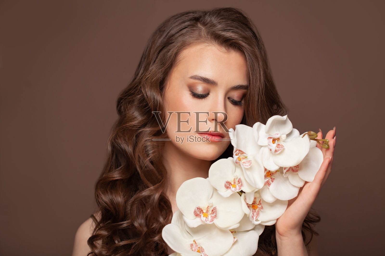 健康的女性，皮肤干净，棕色的卷发和白色的兰花花。美容、护发、护肤理念照片摄影图片