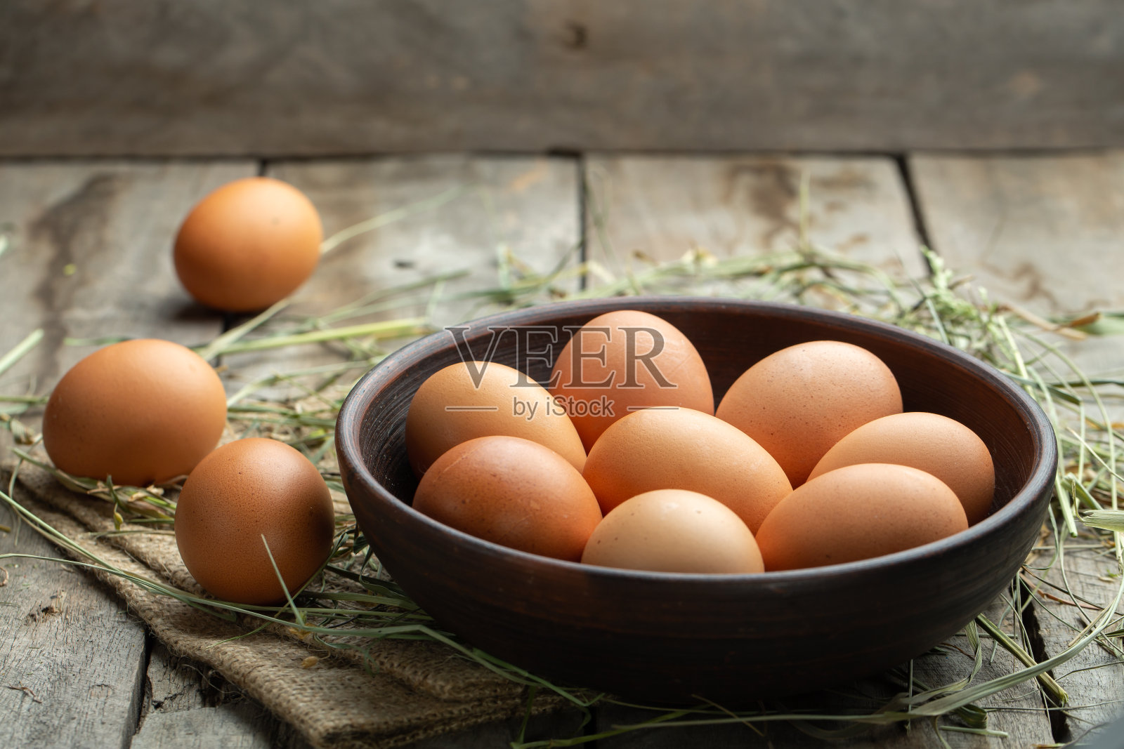 鸡蛋放在泥碗里，木头做背景，干草散落在周围。健康食品的概念。照片摄影图片
