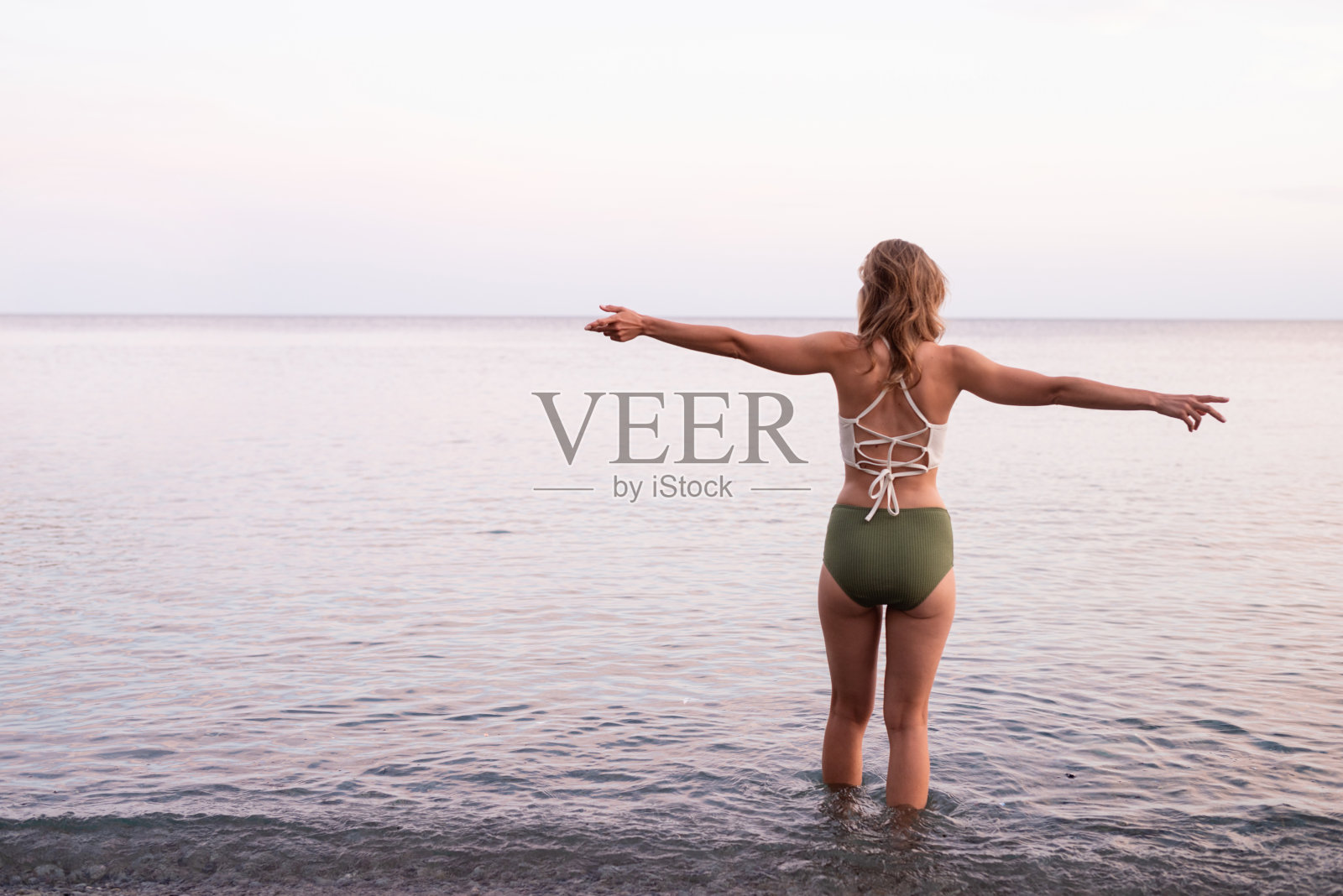 一个年轻女人的后视图站在石头海滩上伸出双臂照片摄影图片
