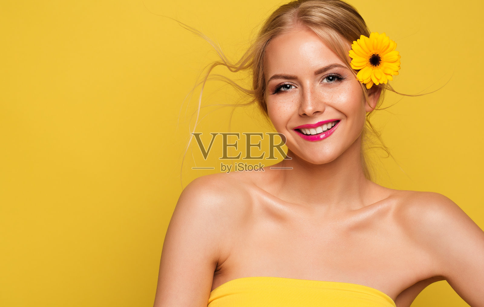 快乐美丽模特女孩在黄色背景。快乐微笑的年轻女人雀斑的脸肖像与花。夏季化妆品皮肤防晒和化妆照片摄影图片