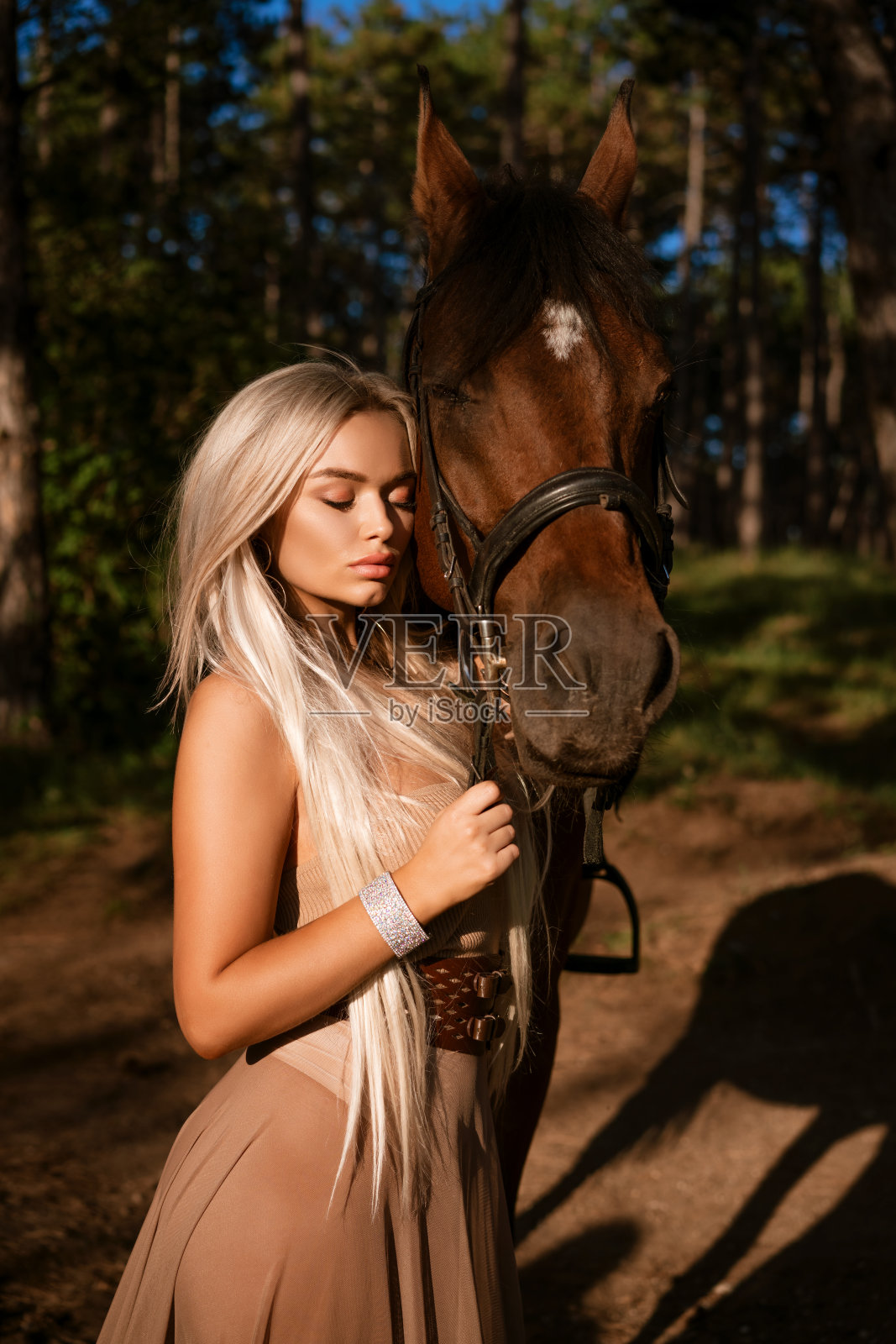 一个漂亮的年轻女人，穿着棕色的裙子，牵着一匹马在公园里照片摄影图片