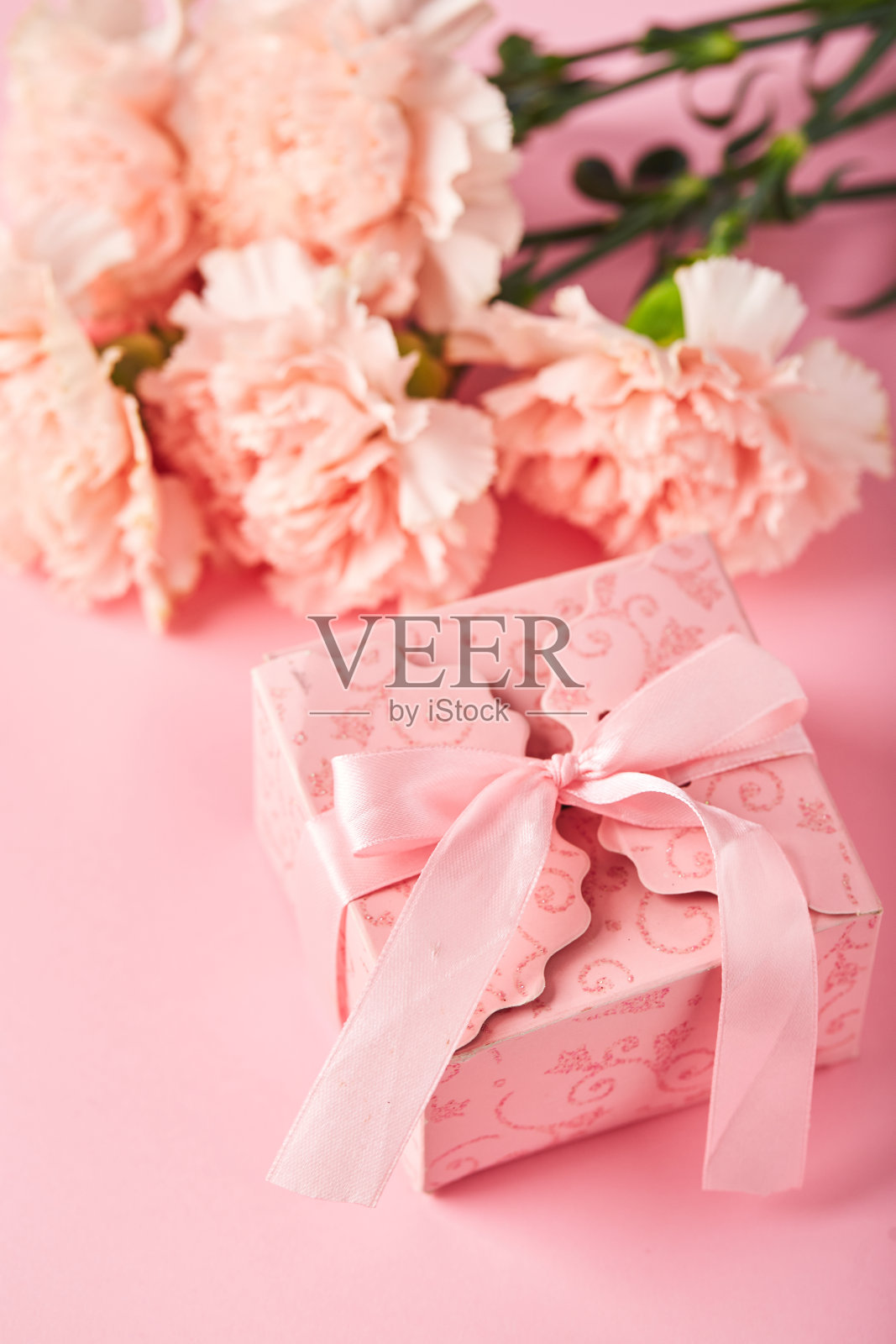 粉色康乃馨和粉色礼盒。粉红色背景上的康乃馨花束是节日问候的设计理念照片摄影图片