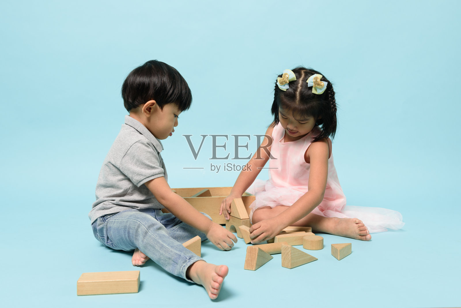 亚洲两个人的孩子一起玩的木头玩具块在淡蓝色背景的工作室。儿童技能，儿童角色与出生顺序，儿童发展概念。照片摄影图片