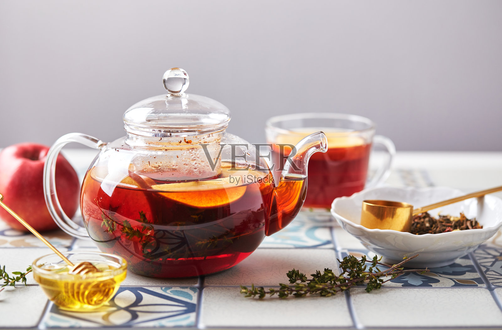 水果茶与苹果和百里香在玻璃茶壶和杯子在彩色瓷砖桌子照片摄影图片
