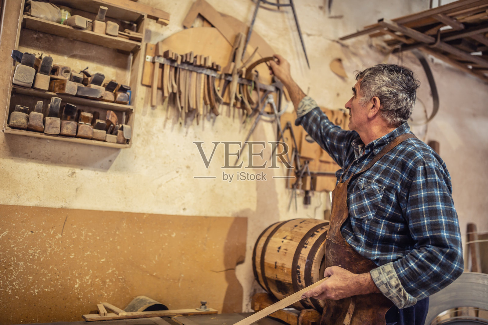 老工匠在一个简陋的作坊里挑选制作木制品所需的零件。照片摄影图片