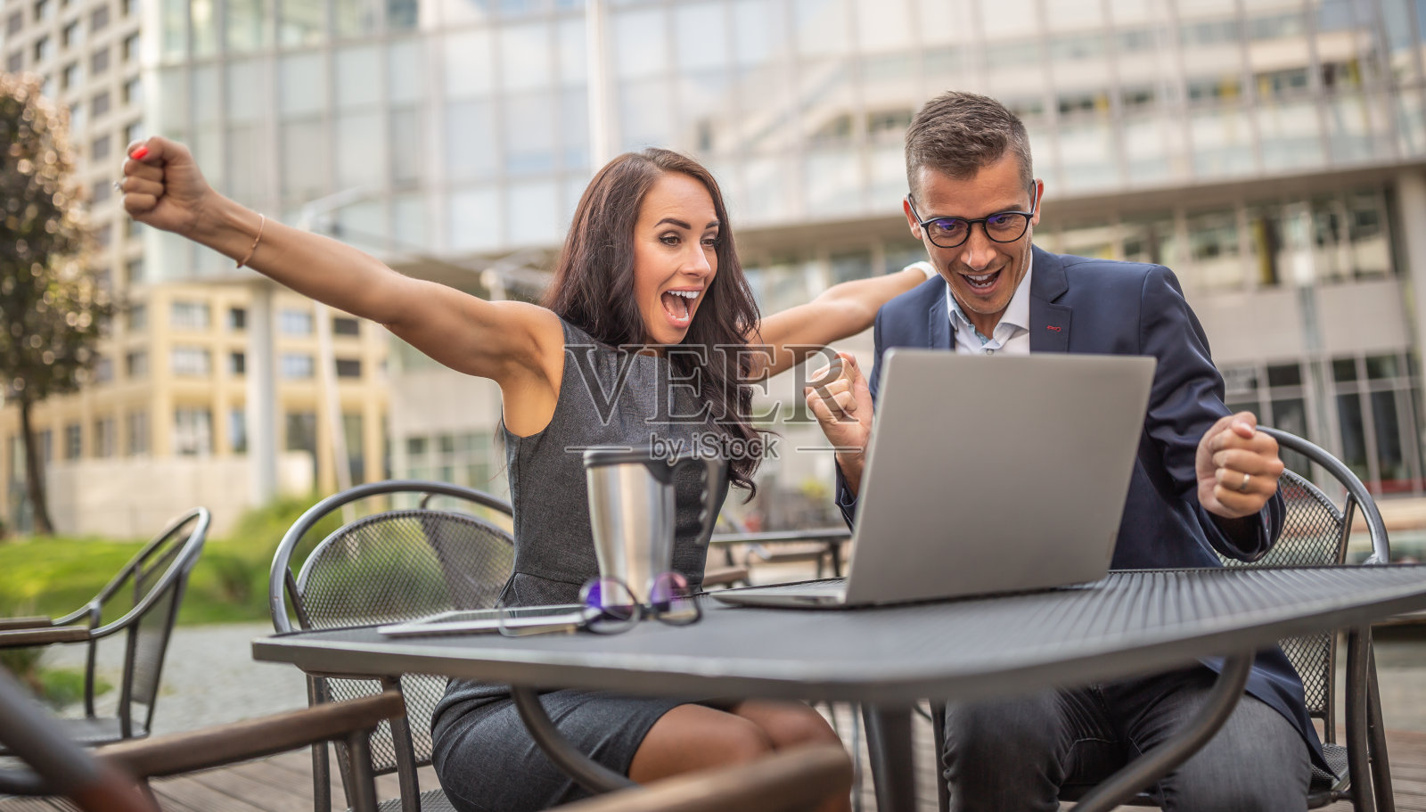 在城市的户外，男男女女同事都对自己面前的笔记本电脑上的成功交易表现出激动的热情。照片摄影图片