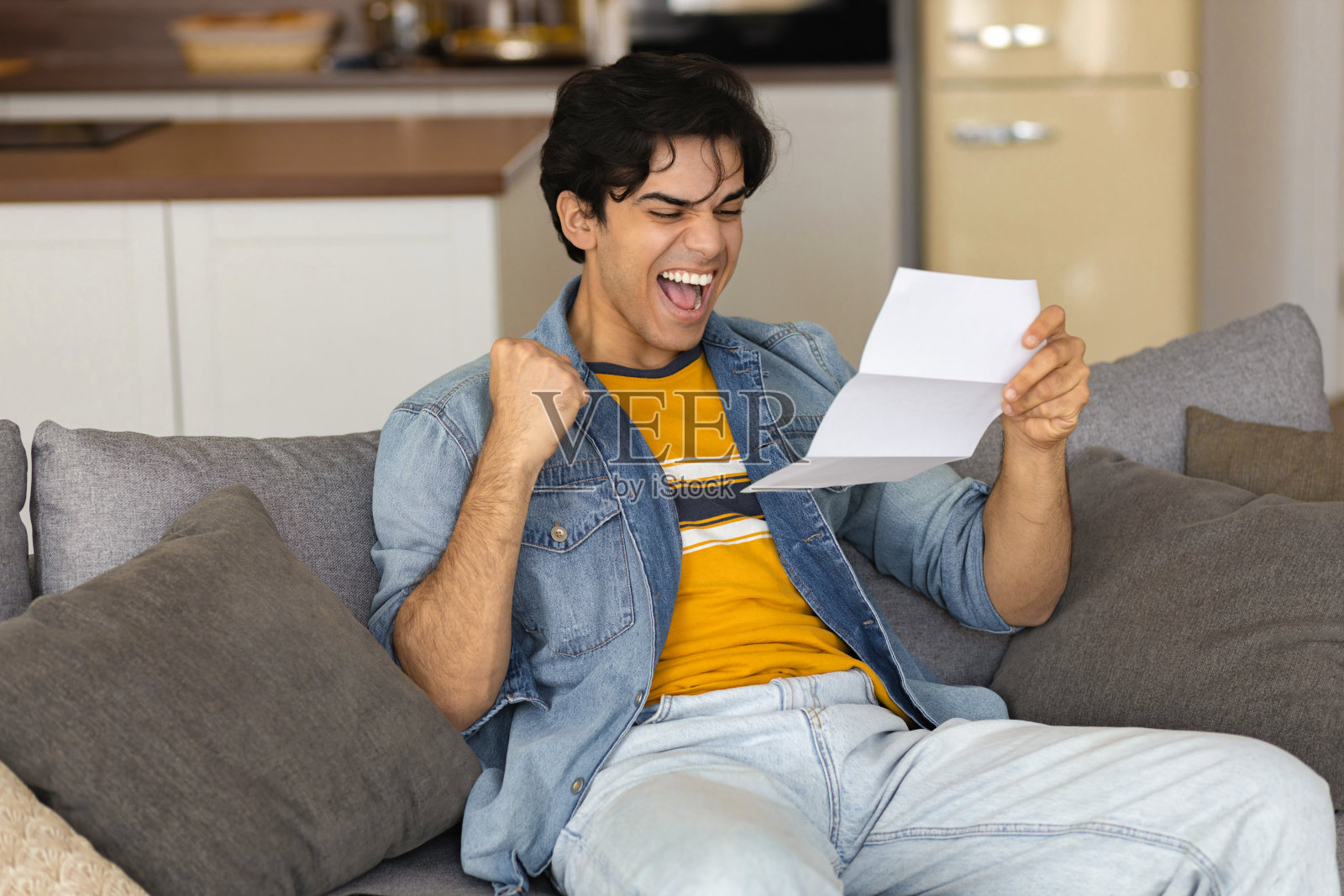 年轻快乐的男人手里拿着一封信，坐在家里的沙发上读着收到的好消息通知照片摄影图片