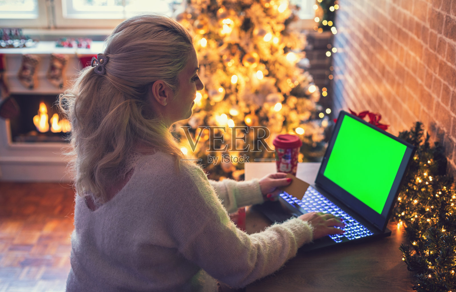 年轻美丽的女人享受舒适的圣诞节气氛，同时使用笔记本电脑在线购物。照片摄影图片