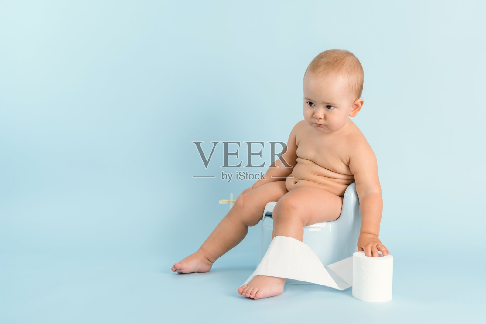一个一岁的孩子正坐在一个塑料罐子上，蓝色的背景上是卫生纸。新生儿如厕训练，复印空间照片摄影图片