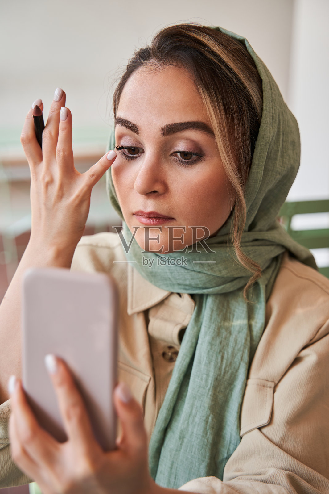 一名戴头巾的伊斯兰妇女一边画睫毛一边看着手机上的自拍相机照片摄影图片