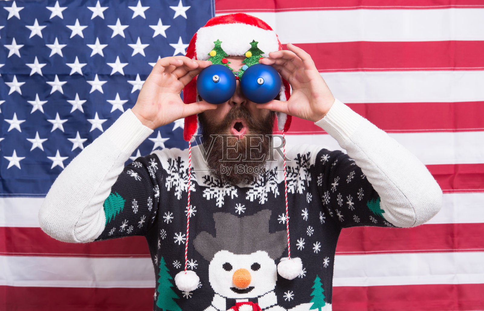 我看着你。长胡子的男人戴着滑稽的眼镜。有趣的景象。有趣的圣诞老人在星条旗的背景。有趣但爱国。节日快乐。圣诞快乐。新年的庆祝活动照片摄影图片