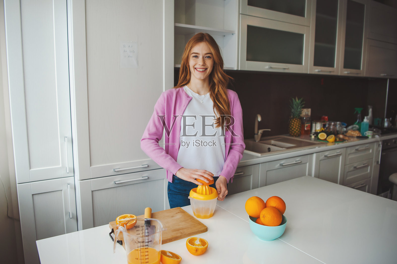 一个女人在厨房里泡橙汁，享受一早上的时光。健康的饮食习惯照片摄影图片
