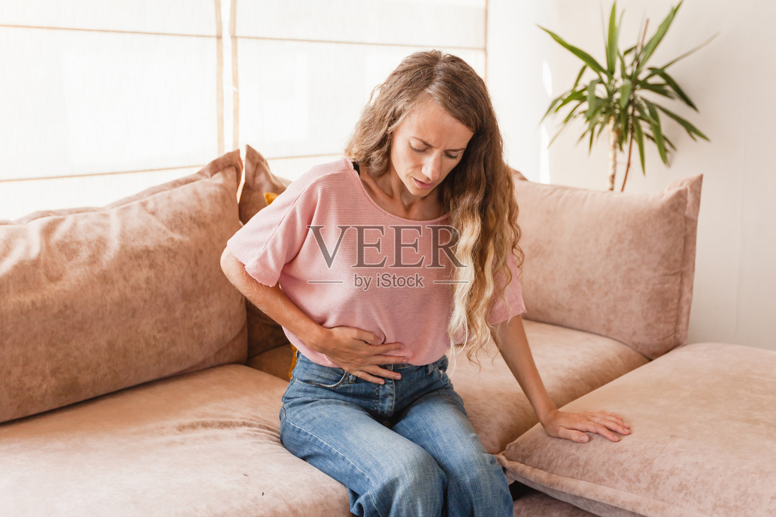 一名年轻女子坐在家里的沙发上，忍受着强烈的腹痛照片摄影图片