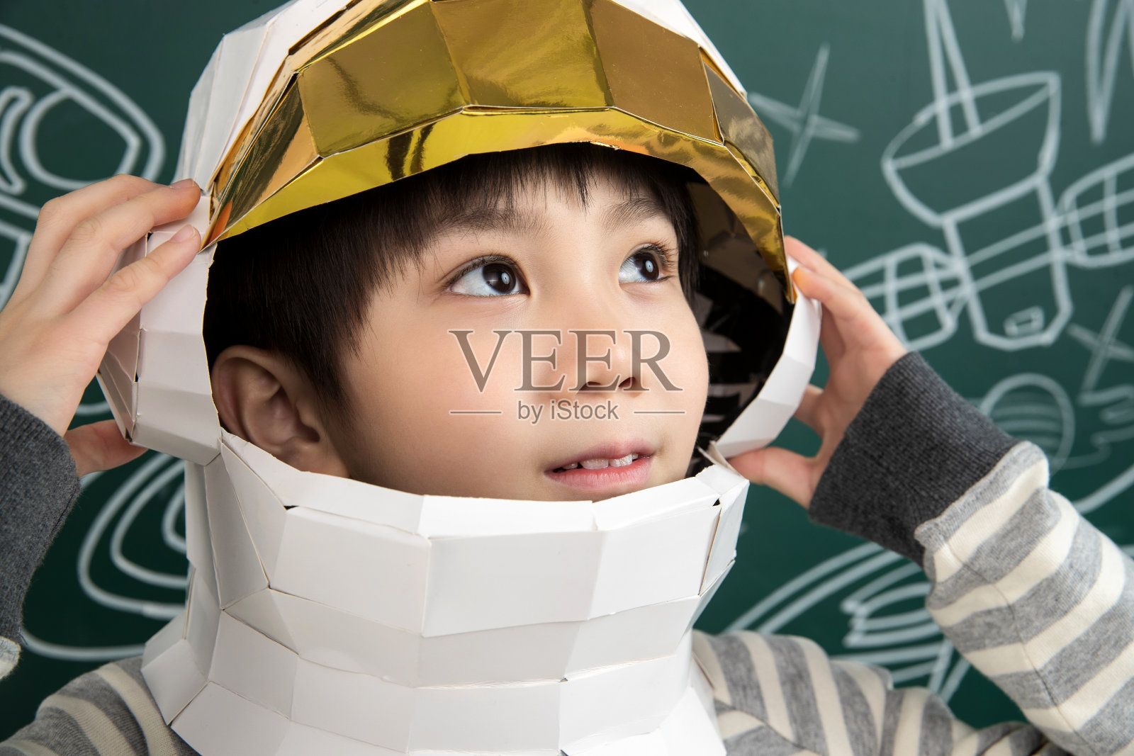 戴着航天员头盔的小男孩站在黑板前照片摄影图片