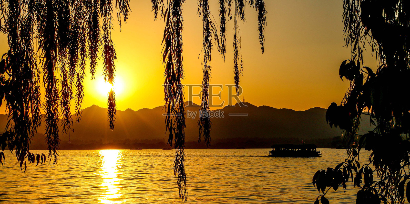 日落景观和杭州西湖的风景，阳光透过落下的柳树树叶照耀，游船穿过湖面的山脉照片摄影图片