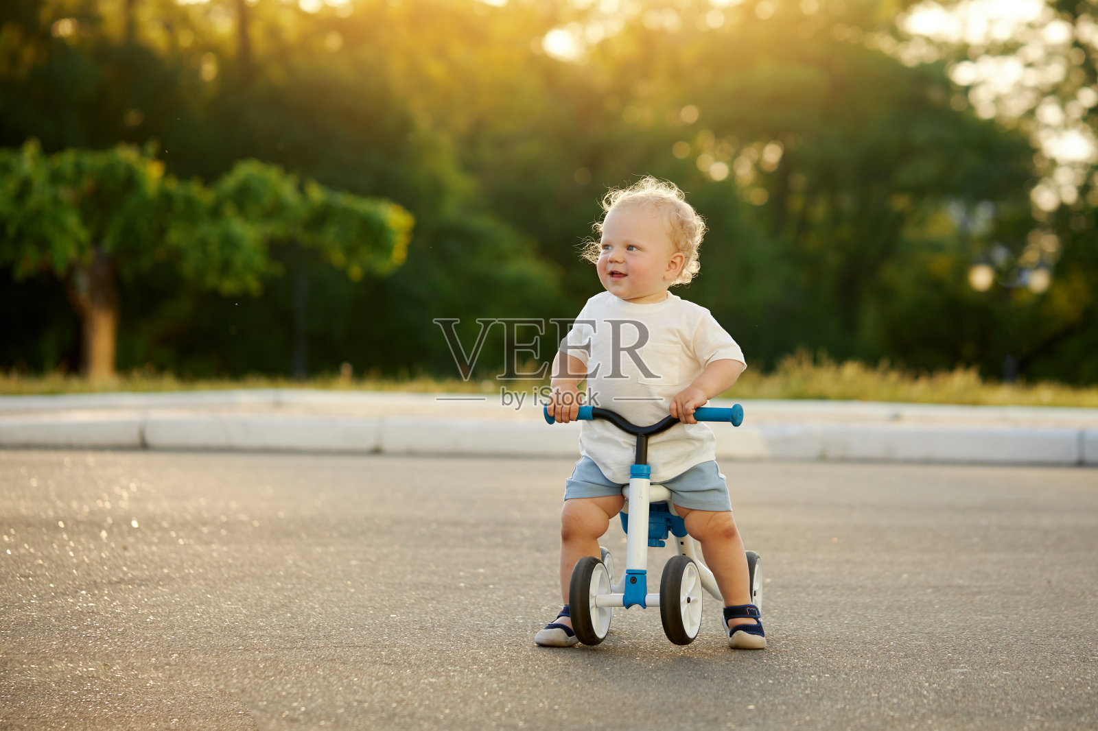 可爱宝宝学骑平衡自行车。一个小孩试图在阳光明媚的公园里骑自行车。那孩子梦想成为一名摩托车手照片摄影图片